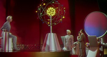 Movie still from “This Island Earth” (1955), directed by Joseph M. Newman – A group of people standing next to a model of an atom; Extreme Wide shot, Low angle