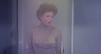 Movie still from “This Island Earth” (1955), directed by Joseph M. Newman – A woman in a gray dress is standing in front of a mirror; Medium shot, Low angle