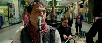 Movie still from “This Must Be the Place” (2011), directed by Paolo Sorrentino – A man is singing into a microphone in front of a crowd; Close Up shot, Over the shoulder angle