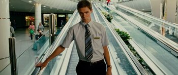 Movie still from “This Must Be the Place” (2011), directed by Paolo Sorrentino – A man in a dress shirt and tie standing in front of an escalator; Medium shot, Low angle