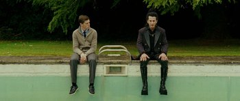 Movie still from “This Must Be the Place” (2011), directed by Paolo Sorrentino – Two young men sitting on a bench next to each other; Wide shot, Low angle