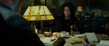 Movie still from “This Must Be the Place” (2011), directed by Paolo Sorrentino – A person sitting at a table with a lamp; Medium shot, Over the shoulder angle