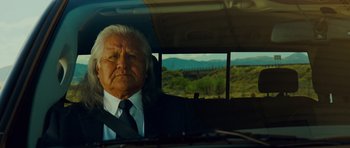 Movie still from “This Must Be the Place” (2011), directed by Paolo Sorrentino – An older man in a suit and tie sitting in the driver's seat of a car; Close Up shot, Over the shoulder angle