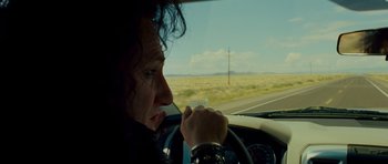 Movie still from “This Must Be the Place” (2011), directed by Paolo Sorrentino – A person sitting in the drivers seat of a car on the side of the road; Close Up shot, Over the shoulder angle