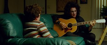 Movie still from “This Must Be the Place” (2011), directed by Paolo Sorrentino – A woman sitting on a couch with a boy playing a guitar; Medium shot, Over the shoulder angle