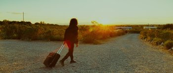 Movie still from “This Must Be the Place” (2011), directed by Paolo Sorrentino – A woman walking down a gravel road with a suitcase; Wide shot, Low angle