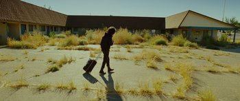 Movie still from “This Must Be the Place” (2011), directed by Paolo Sorrentino – A person walking with a suitcase in the middle of an empty lot; Wide shot, Low angle