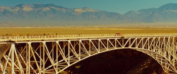 Movie still from “This Must Be the Place” (2011), directed by Paolo Sorrentino – A bridge that is over a river with a mountain in the background; Extreme Wide shot, Low angle