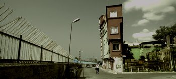 Movie still from “Three Monkeys” (2008), directed by Nuri Bilge Ceylan – A person walking down a street near a tall building; Extreme Wide shot, Low angle