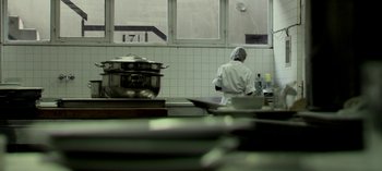 Movie still from “Three Monkeys” (2008), directed by Nuri Bilge Ceylan – A person standing in a kitchen preparing a meal; Medium shot, Low angle
