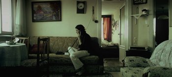 Movie still from “Three Monkeys” (2008), directed by Nuri Bilge Ceylan – A woman sitting on top of a couch talking on the phone; Wide shot, High angle