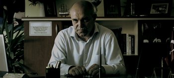 Movie still from “Three Monkeys” (2008), directed by Nuri Bilge Ceylan – A man sitting at a table with a knife in front of him; Close Up shot, Low angle
