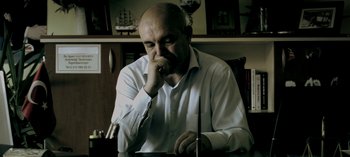 Movie still from “Three Monkeys” (2008), directed by Nuri Bilge Ceylan – An older man sitting at a table in front of a book; Close Up shot, Low angle