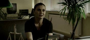 Movie still from “Three Monkeys” (2008), directed by Nuri Bilge Ceylan – A woman sitting at a table in front of a plant; Close Up shot, Over the shoulder angle