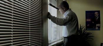 Movie still from “Three Monkeys” (2008), directed by Nuri Bilge Ceylan – A man standing in front of a window looking out of the blinds; Medium shot, Low angle
