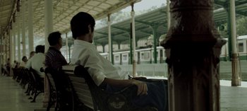 Movie still from “Three Monkeys” (2008), directed by Nuri Bilge Ceylan – A man sitting on top of a bench near a train platform; Wide shot, High angle