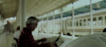 Movie still from “Three Monkeys” (2008), directed by Nuri Bilge Ceylan – A man reading a newspaper while sitting in a train station; Extreme Close Up shot, Low angle