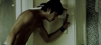 Movie still from “Three Monkeys” (2008), directed by Nuri Bilge Ceylan – A shirtless man leaning against a wall with his hand on the wall; Close Up shot, Overhead angle