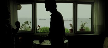 Movie still from “Three Monkeys” (2008), directed by Nuri Bilge Ceylan – A man standing in front of a large window; Medium shot, Over the shoulder angle
