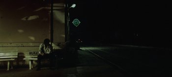 Movie still from “Three Monkeys” (2008), directed by Nuri Bilge Ceylan – A person sitting on a bench near a street sign; Extreme Wide shot, Low angle