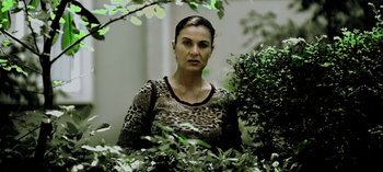 Movie still from “Three Monkeys” (2008), directed by Nuri Bilge Ceylan – A woman in a leopard print shirt standing in a bush; Medium shot, High angle