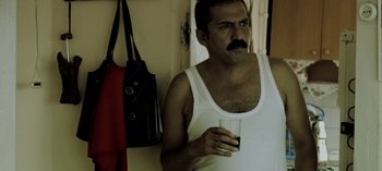 Movie still from “Three Monkeys” (2008), directed by Nuri Bilge Ceylan – A man in a white tank top holding a glass of water; Medium shot, High angle