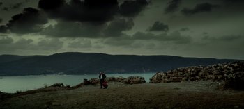 Movie still from “Three Monkeys” (2008), directed by Nuri Bilge Ceylan – A man standing on top of a sandy beach near a body of water under a cloudy sky; Extreme Wide shot, Low angle