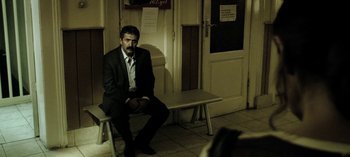 Movie still from “Three Monkeys” (2008), directed by Nuri Bilge Ceylan – A man in a suit sitting on top of a wooden bench; Wide shot, High angle