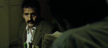 Movie still from “Three Monkeys” (2008), directed by Nuri Bilge Ceylan – A man wearing a suit and tie in a dark room; Close Up shot, Over the shoulder angle