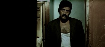 Movie still from “Three Monkeys” (2008), directed by Nuri Bilge Ceylan – A man with a beard wearing a jacket and a white shirt; Medium shot, Low angle