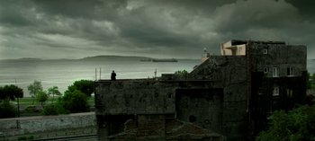 Movie still from “Three Monkeys” (2008), directed by Nuri Bilge Ceylan – A man sitting on a wall looking out at the ocean; Extreme Wide shot, Low angle