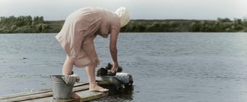 Movie still from “Three Poplars on Plyuschikha Street” (1968), directed by Tatyana Lioznova – An older woman standing on a pier with a boat; Wide shot, High angle