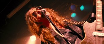 Movie still from “Tideland” (2005), directed by Terry Gilliam – A person with long hair and sunglasses holding a microphone; Close Up shot, Low angle