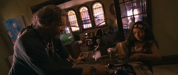 Movie still from “Tideland” (2005), directed by Terry Gilliam – A person sitting at a table in front of a window; Medium shot, Low angle