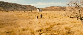 Movie still from “Tideland” (2005), directed by Terry Gilliam – Two people walking through a dry grass field with a house in the background; Extreme Wide shot, High angle