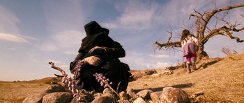 Movie still from “Tideland” (2005), directed by Terry Gilliam – A person sitting on the ground near a tree; Wide shot, Low angle