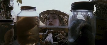 Movie still from “Tideland” (2005), directed by Terry Gilliam – A young girl wearing a straw hat looking into a jar of pinecones; Close Up shot, Over the shoulder angle