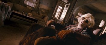 Movie still from “Tideland” (2005), directed by Terry Gilliam – A woman sitting on top of a couch next to a window; Wide shot, Low angle