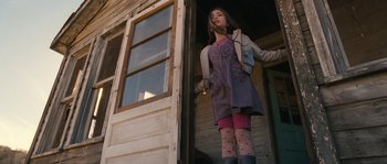 Movie still from “Tideland” (2005), directed by Terry Gilliam – A woman standing in front of an open door of a house; Medium shot, Low angle
