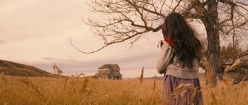 Movie still from “Tideland” (2005), directed by Terry Gilliam – A woman standing in front of an abandoned house in a field; Wide shot, Low angle
