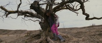 Movie still from “Tideland” (2005), directed by Terry Gilliam – A young girl leaning against a tree in a field; Wide shot, Low angle