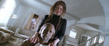Movie still from “Tideland” (2005), directed by Terry Gilliam – A woman with dreadlocks standing next to a statue of an old man; Close Up shot, Low angle