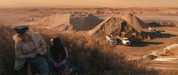 Movie still from “Tideland” (2005), directed by Terry Gilliam – Two women sitting on a hill overlooking a large open pit; Extreme Wide shot, High angle