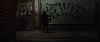 Movie still from “Tigers Are Not Afraid” (2017), directed by Issa López – A person standing in front of a wall with a cat painted on it; Wide shot, Low angle