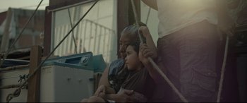 Movie still from “Tigers Are Not Afraid” (2017), directed by Issa López – An older man holding a young girl while sitting on top of a swing; Medium shot, Low angle