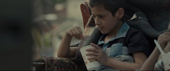Movie still from “Tigers Are Not Afraid” (2017), directed by Issa López – A boy sitting on a chair holding a cup of coffee; Close Up shot, High angle