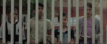 Movie still from “Tigers Are Not Afraid” (2017), directed by Issa López – A group of young boys standing next to each other behind bars; Medium shot, Low angle
