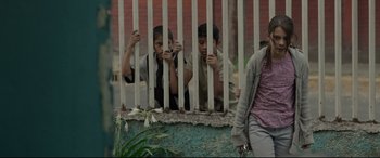 Movie still from “Tigers Are Not Afraid” (2017), directed by Issa López – A group of young men standing next to each other behind a fence; Medium shot, Low angle