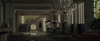 Movie still from “Tigers Are Not Afraid” (2017), directed by Issa López – A person standing in a room with stairs and a chandelier; Extreme Wide shot, Low angle