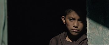 Movie still from “Tigers Are Not Afraid” (2017), directed by Issa López – A young boy with a black shirt on looking at the camera; Close Up shot, Low angle